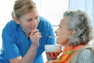 Image of a person assisting an elderly woman to eat.