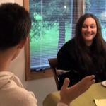 Image of a man and a woman sitting at a table. The man is speaking while the woman looks at him, smiling.